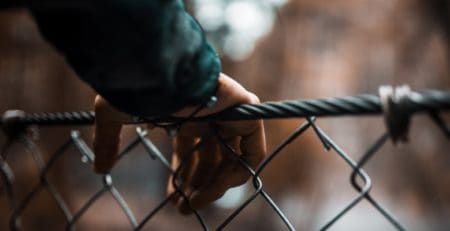 Child's hand gripping a chain-link fence in an outdoor setting.