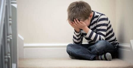 Child sitting on the floor with hands over face, showing distress or anxiety.